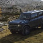 A black 2021 Ford Bronco 2dr is off-roading on a grassy mountainside.