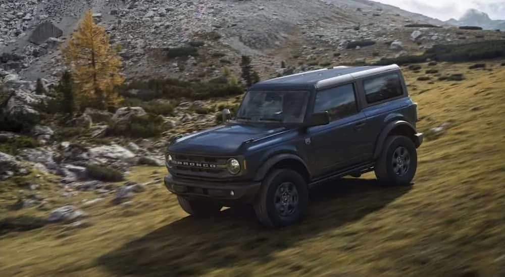 A black 2021 Ford Bronco 2dr is off-roading on a grassy mountainside.