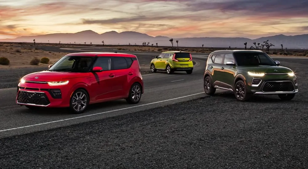 A red, a bright green, and a dark green 2021 Kia Soul are parked on a desert road.