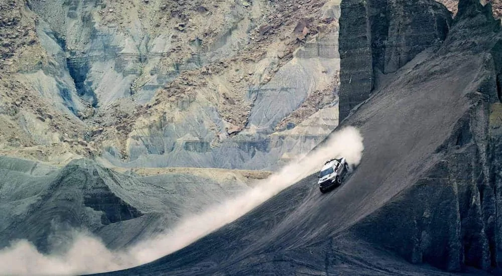 A silver 2021 Ram 1500 TRX is off-roading up a rock formation in a quarry, kicking up sand.