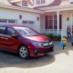 A family is walking toward a red 2020 Honda Odyssey EX outside a white house after leaving a Honda dealer near me.
