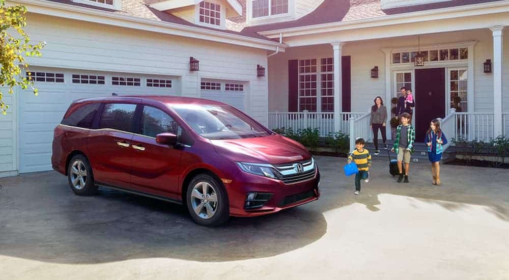 A family is walking toward a red 2020 Honda Odyssey EX outside a white house after leaving a Honda dealer near me.