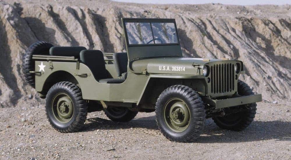 A green 1940s Jeep Willys is parked in a gravel pit.