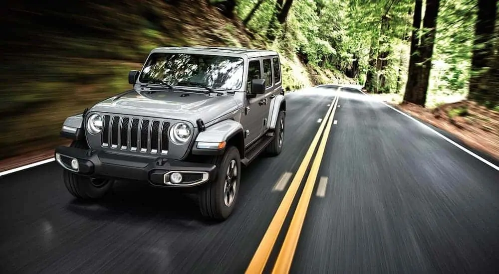 A 2019 used Jeep Wrangler is driving on a tree-lined road.