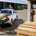 Workers are loading wood into the bed of a 2018 Ram 1500 at a lumber yard.
