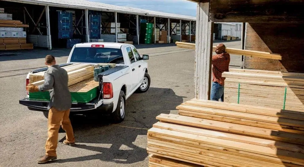 Workers are loading wood into the bed of a 2018 Ram 1500 at a lumber yard.