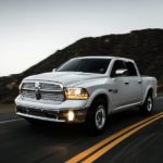 A silver 2015 used Ram 1500 is driving down the road.