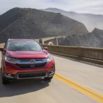 A red 2018 used Honda CRV is driving over a bridge overlooking the mountains and ocean.