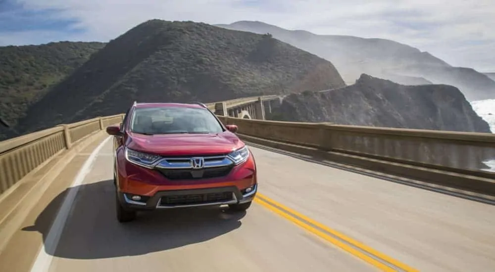 A red 2018 used Honda CRV is driving over a bridge overlooking the mountains and ocean.