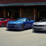 Four 2021 Chevrolet Camaros a silver, a blue, a red, and a white are all parked in front of a warehouse.