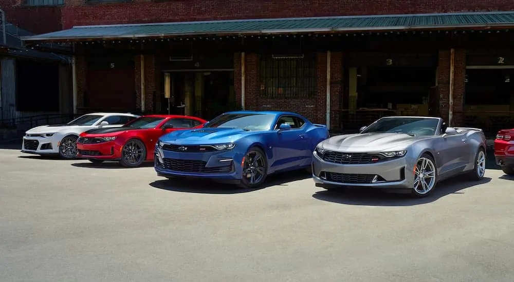 Four 2021 Chevrolet Camaros a silver, a blue, a red, and a white are all parked in front of a warehouse.