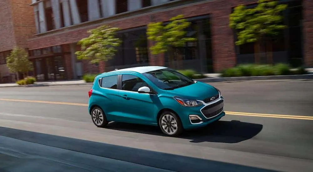 A blue and white 2021 Chevy Spark is driving down a city street.