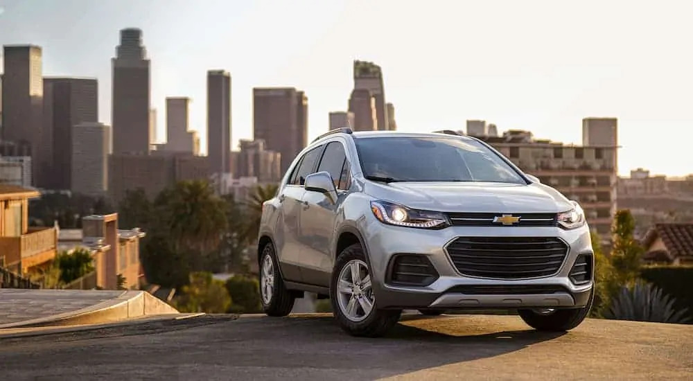 A silver 2021 Chevy Trax is parked on a hill with a city in the background.