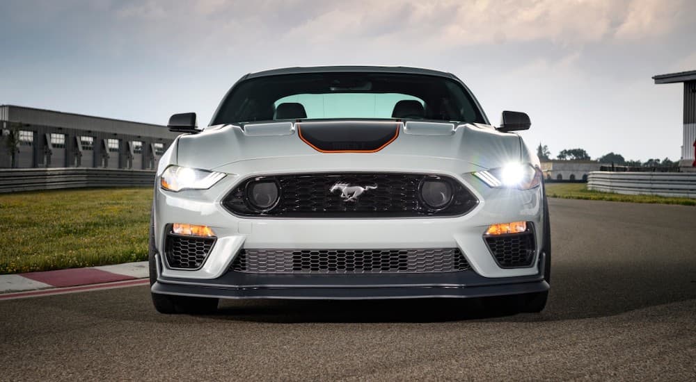 A white 2021 Ford Mustang Mach 1 is parked at the track with its headlights illuminated.