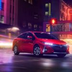 A red 2021 Toyota Prius Prime Limited is parked on a city street with neon lights in the background.