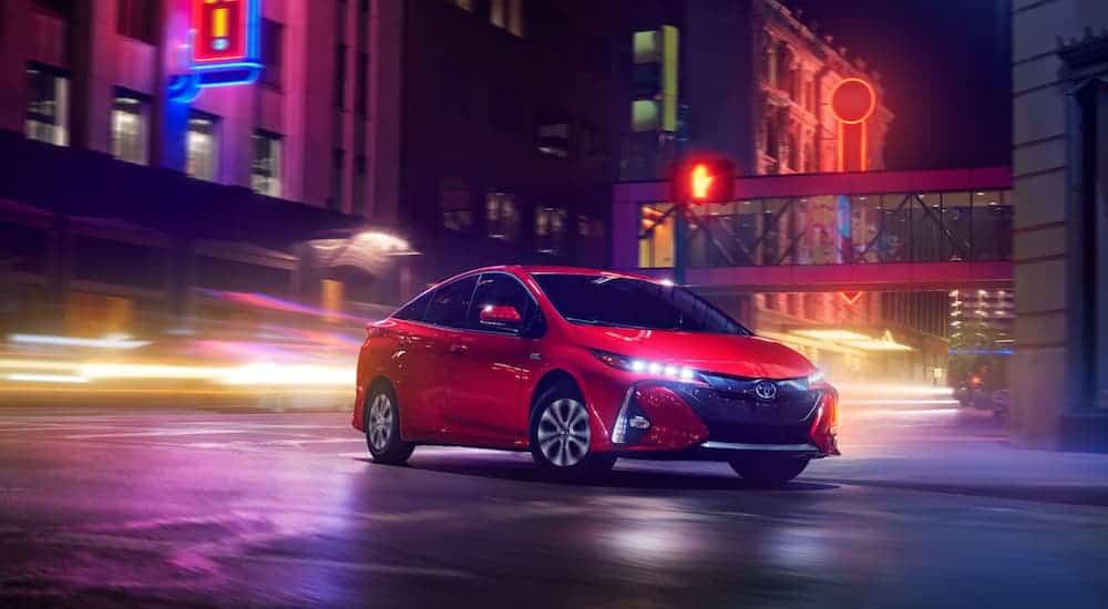 A red 2021 Toyota Prius Prime Limited is parked on a city street with neon lights in the background.