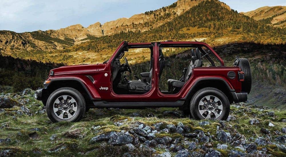 A burgundy 2021 Jeep Wrangler Sahara Unlimited is parked in the mountains with its doors and top off.