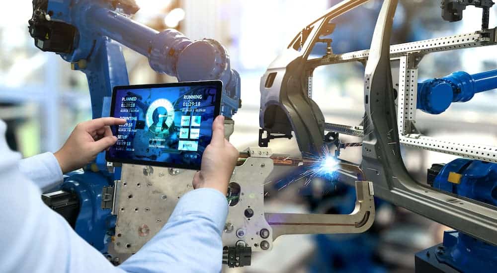 A man with a tablet is monitoring frame welding automation.