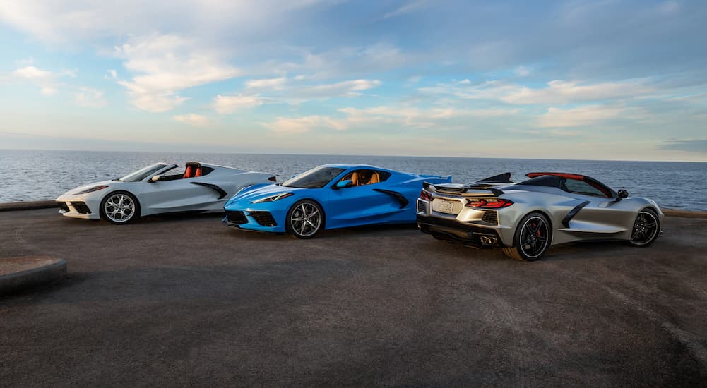 A white, a blue, and a silver 2021 Chevy Corvette are parked in front of the ocean.