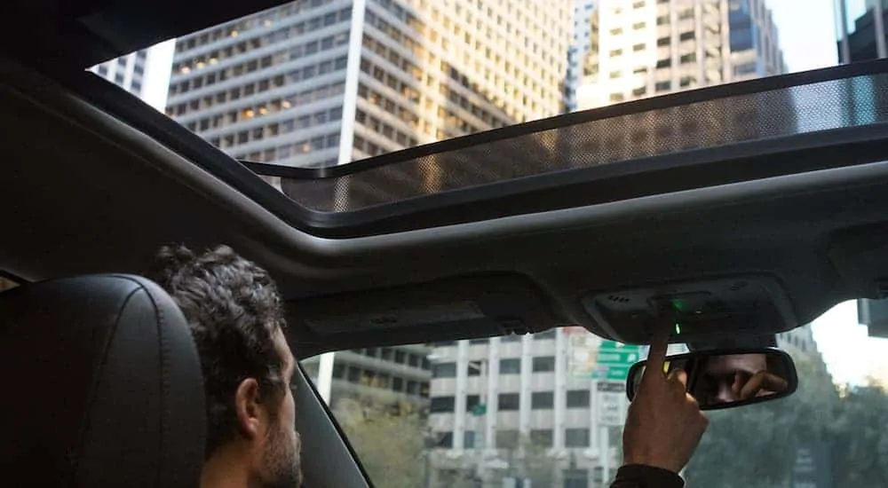 A view from the back seat of a man opening the sunroof in a 2021 Chevy Malibu.