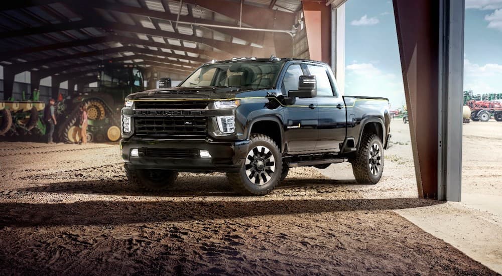 A black 2021 Chevy Silverado 2500 Carhartt Edition is parked in the open garage door of a tractor storage building.