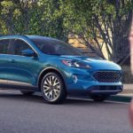 A blue 2021 Ford Escape is shown from the front, angled right and parked on the street with a woman in the foreground.