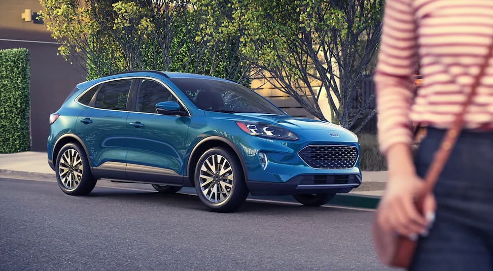 A blue 2021 Ford Escape is shown from the front, angled right and parked on the street with a woman in the foreground.