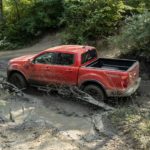 A red 2021 Ford Ranger Tremor Lariat is driving though the mud in the woods.