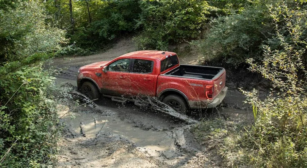 A red 2021 Ford Ranger Tremor Lariat is driving though the mud in the woods.