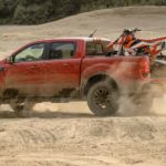 A red 2021 Ford Ranger Tremor Lariat is driving through the dunes with a dirt bike in the bed after the 2021 Ford Ranger vs 2020 Ford Ranger comparison.