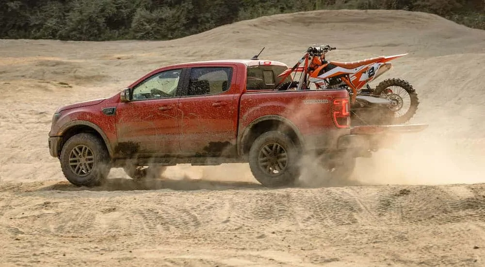 A red 2021 Ford Ranger Tremor Lariat is driving through the dunes with a dirt bike in the bed after the 2021 Ford Ranger vs 2020 Ford Ranger comparison.