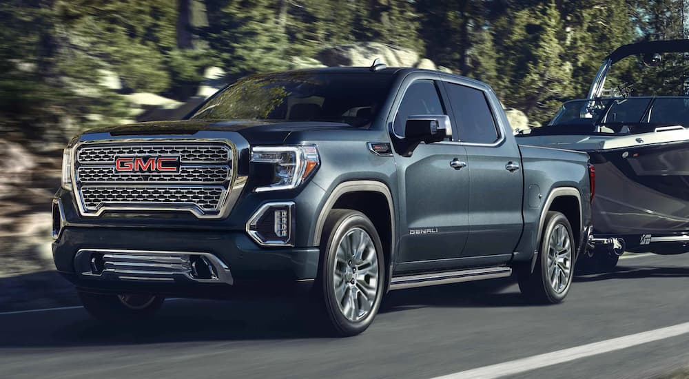 A grey 2021 GMC Sierra 1500 is towing a boat past trees.