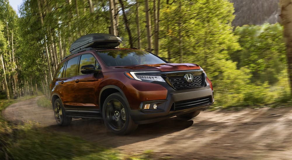 A red 2021 Honda Passport Elite is driving on a dirt road in the woods.