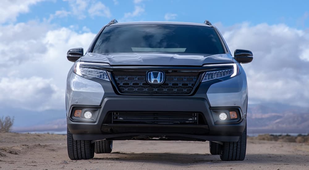 A silver 2021 Honda Passport Elite is shown from the front in front of a blue sky with clouds after winning the 2021 Honda Passport vs 2021 Nissan Pathfinder comparison.