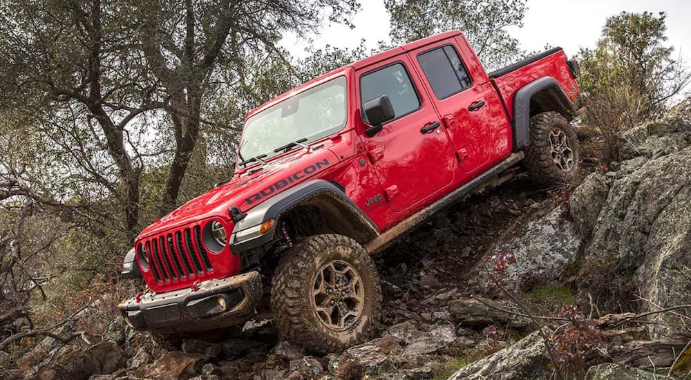 A red 2021 Jeep Gladiator Rubicon is off-roading in the mud on a rocky trail.