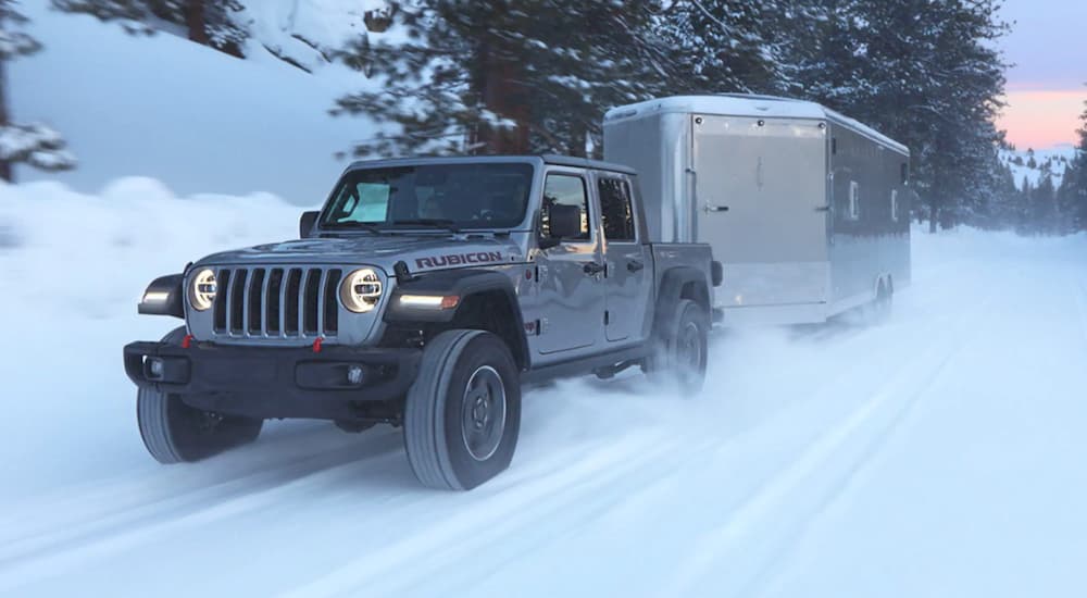 A silver 2021 Jeep Gladiator Rubicon is towing an enclosed trailer on a snowy road.
