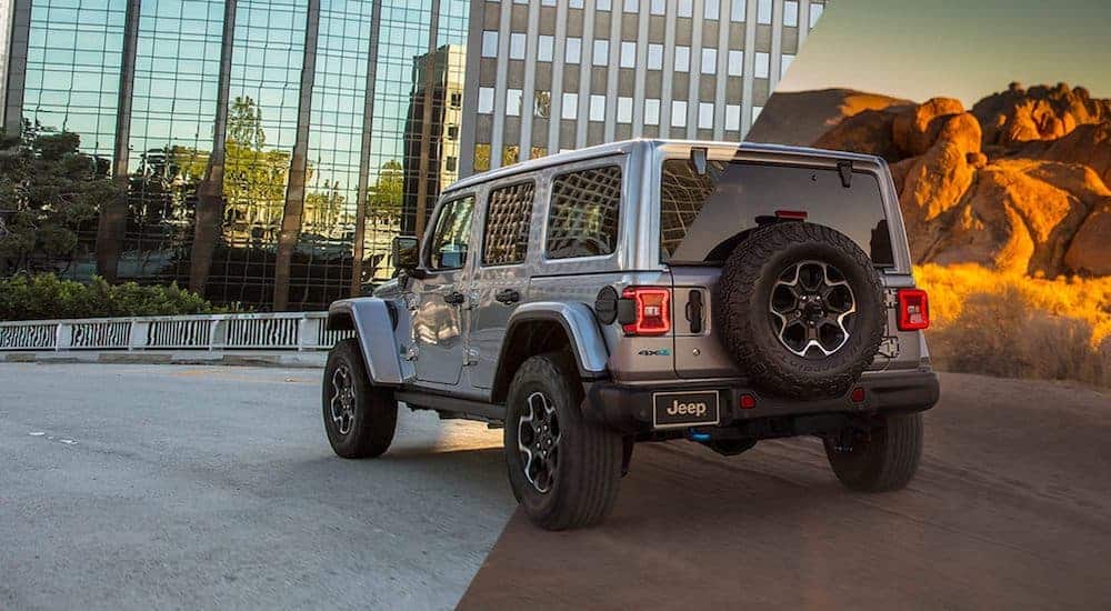 A silver 2021 Jeep Wrangler Rubicon 4xe is shown from behind, half in the city and half in the desert.