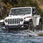 A white 2021 Jeep Wrangler Rubicon is driving through a river.