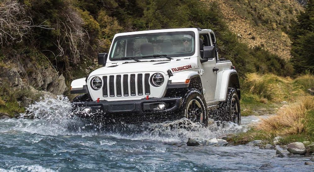 A white 2021 Jeep Wrangler Rubicon is driving through a river.