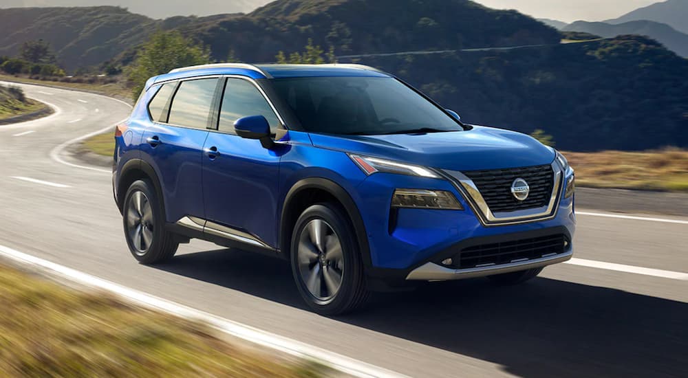 A blue 2021 Nissan Rogue is driving on a winding road.