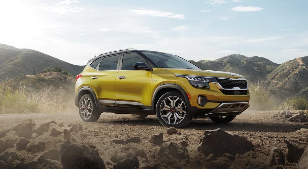 A yellow 2021 Kia Seltos is parked on dirt in front of mountains after winning the 2021 Kia Seltos vs 2021 Nissan Rogue comparison.