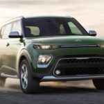 A green 2021 Kia Soul is driving on a desert road at sunset.