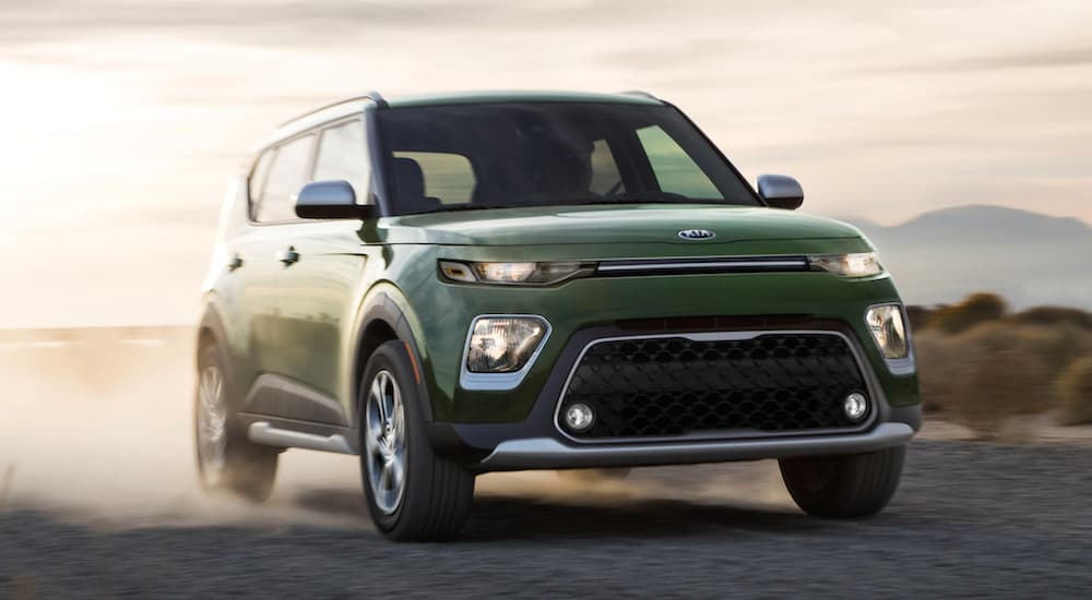 A green 2021 Kia Soul is driving on a desert road at sunset.