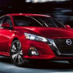 A red 2021 Nissan Altima is shown driving through a city at night.