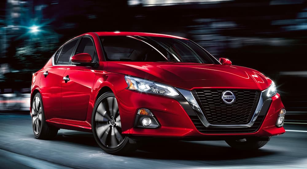 A red 2021 Nissan Altima is shown driving through a city at night.