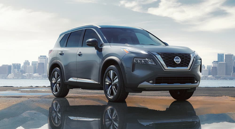 A silver 2021 Nissan Rogue is parked on wet pavement in front of a city skyline.