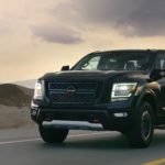 A black 2021 Nissan Titan is driving on an empty highway at dusk.