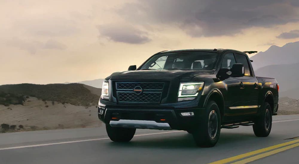 A black 2021 Nissan Titan is driving on an empty highway at dusk.