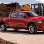 A red 2021 Ram 1500 is having its bed filled with mulch from a front loader.