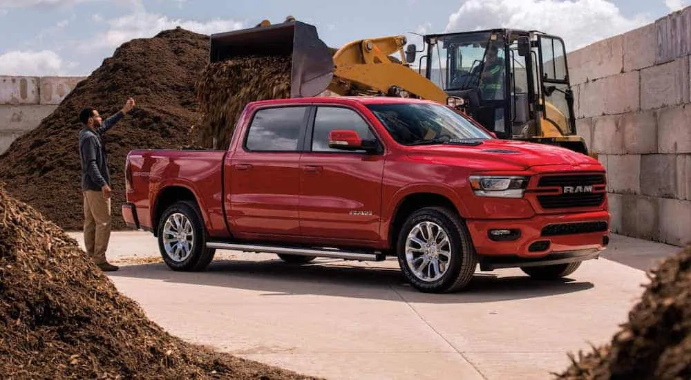 A red 2021 Ram 1500 is having its bed filled with mulch from a front loader.